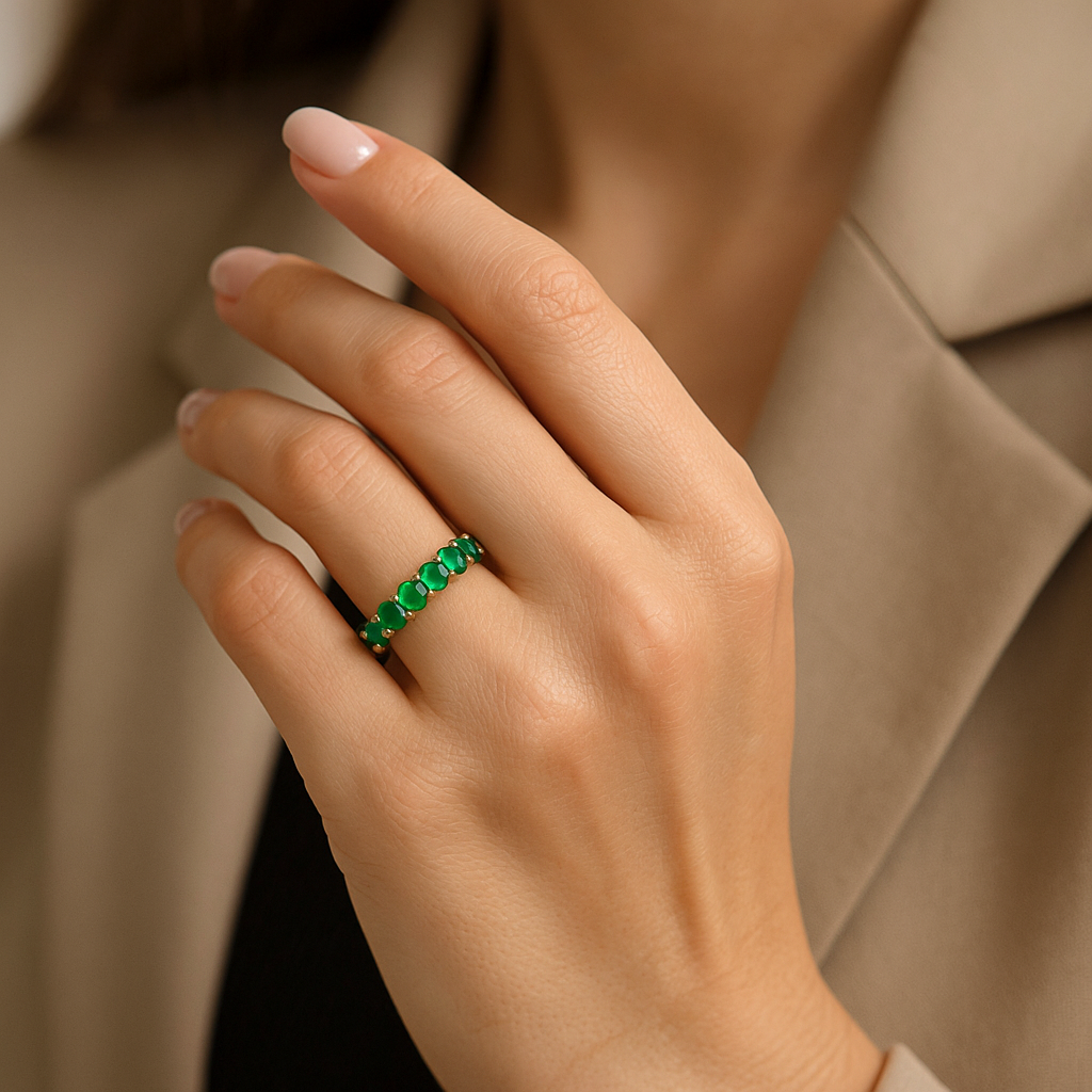 Merginos ranka su prabangiu žiedu juostele iš geltono aukso, inkrustuotu žaliais smaragdais ir baltais deimantais, pabrėžiančiais akmenų grožį