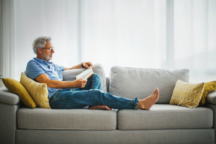 Mature dad reading a book on the sofa.