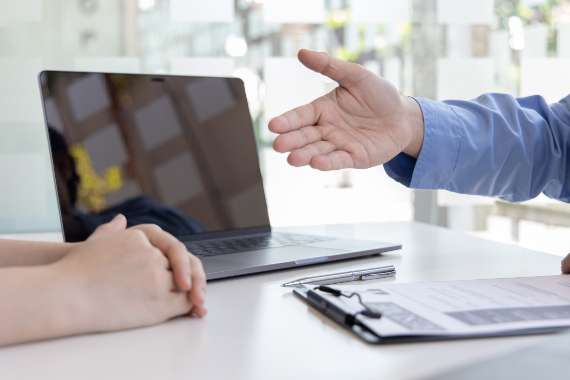 Business broker reaching out to client across desk with laptop and documents