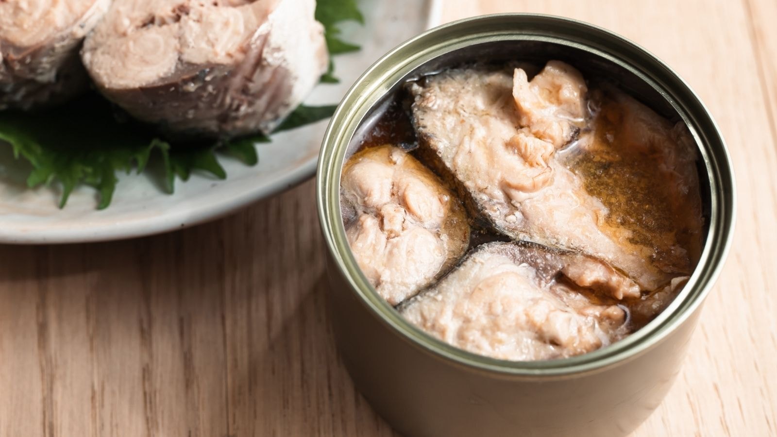 Canned mackerel fillets in oil inside an open tin on wooden table