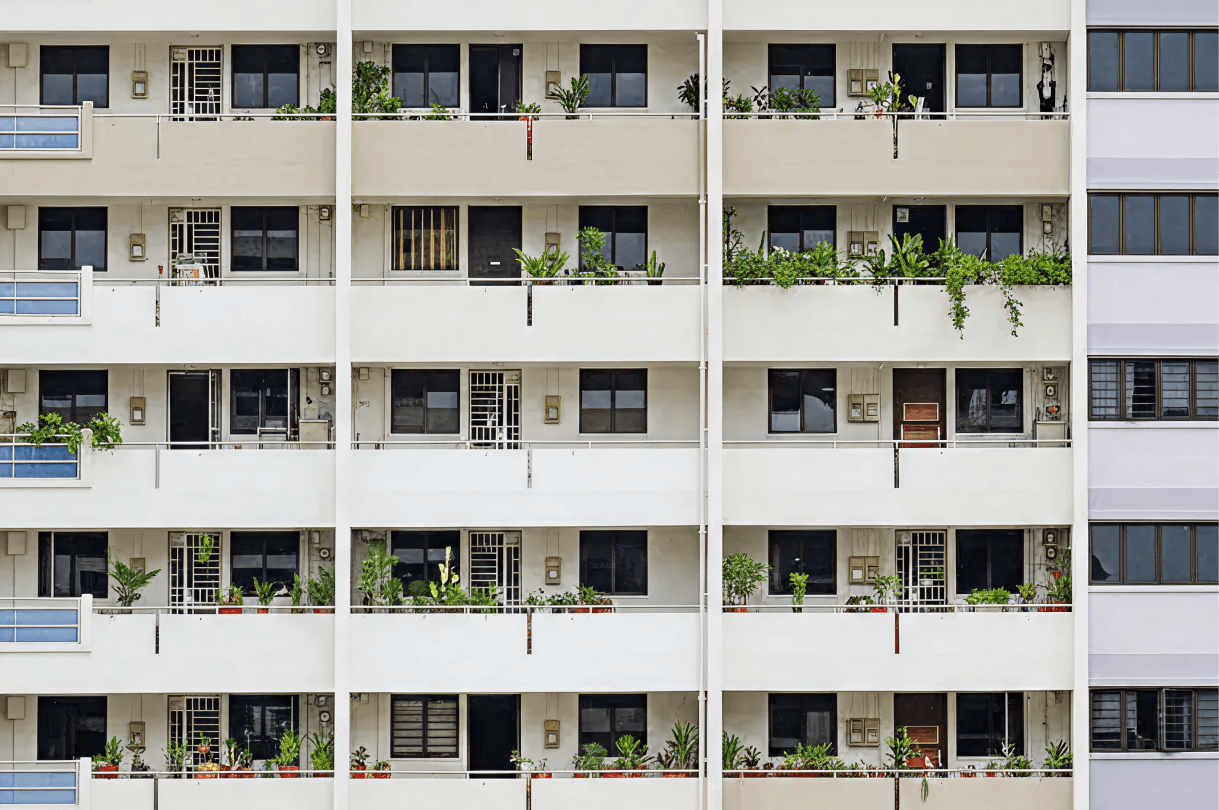 Apartment building facade with repeating balconies, windows, and potted plants.
