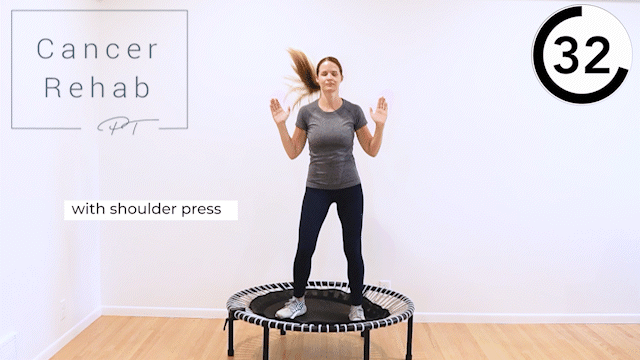 A woman shifting her weight from side to side on a rebounder trampoline, while doing shoulder presses.