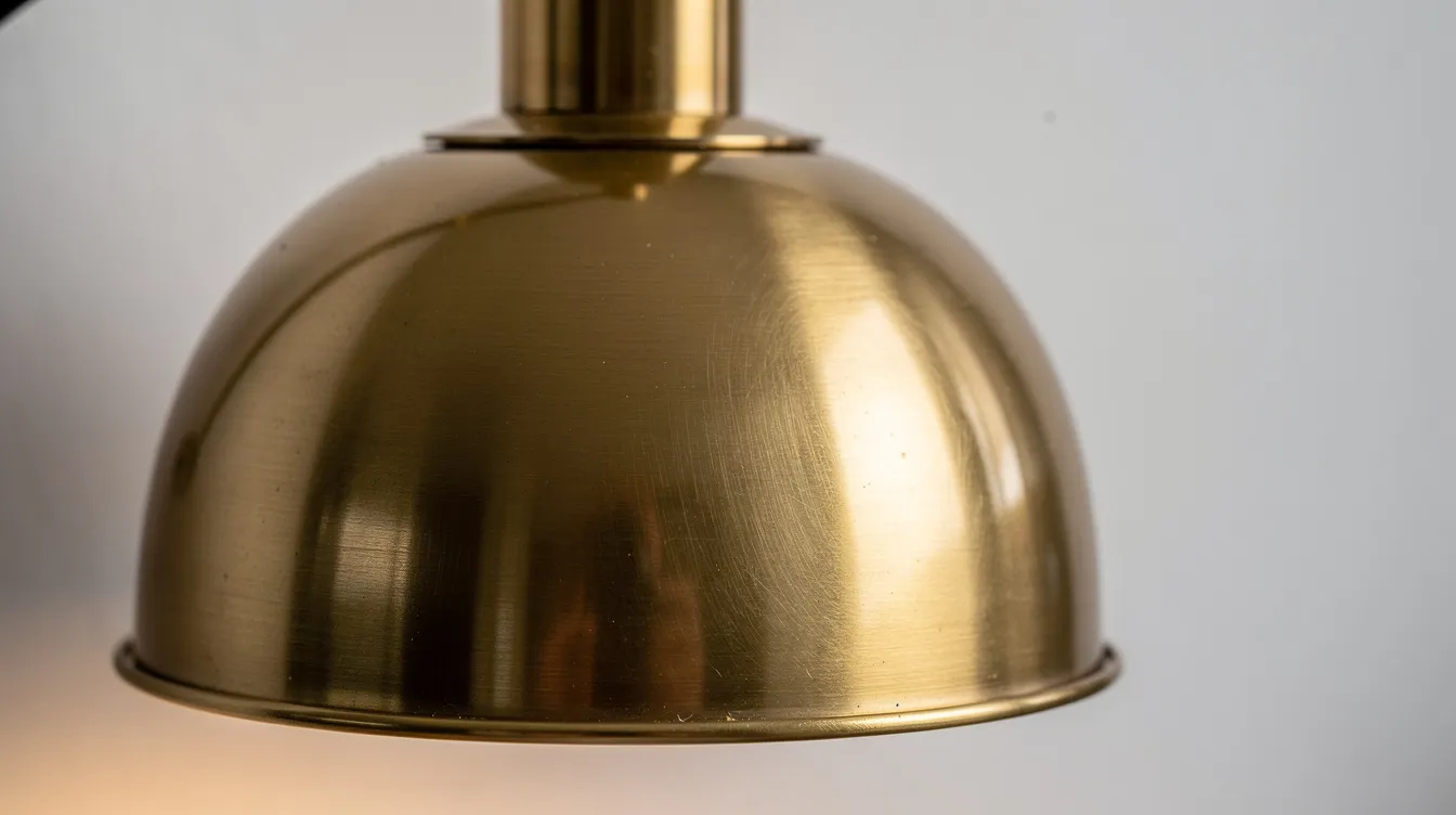 Närbild på en borstad mässingslampa som avger ett varmt ljus mot en vit vägg, vilket skapar en inbjudande atmosfär i rummet. Lampan, som är tillverkad av metall, visar på en stilren design som passar perfekt i hemmet.