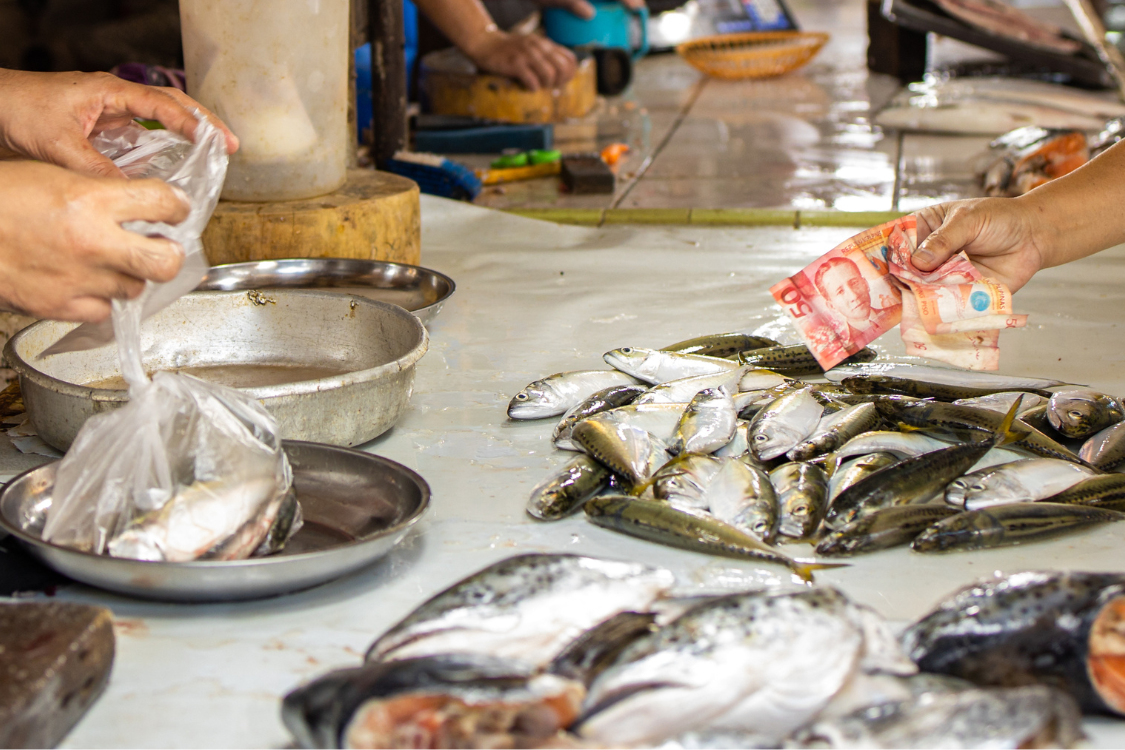 Buyer handing money at a wet market in the Philippines, representing daily living expenses