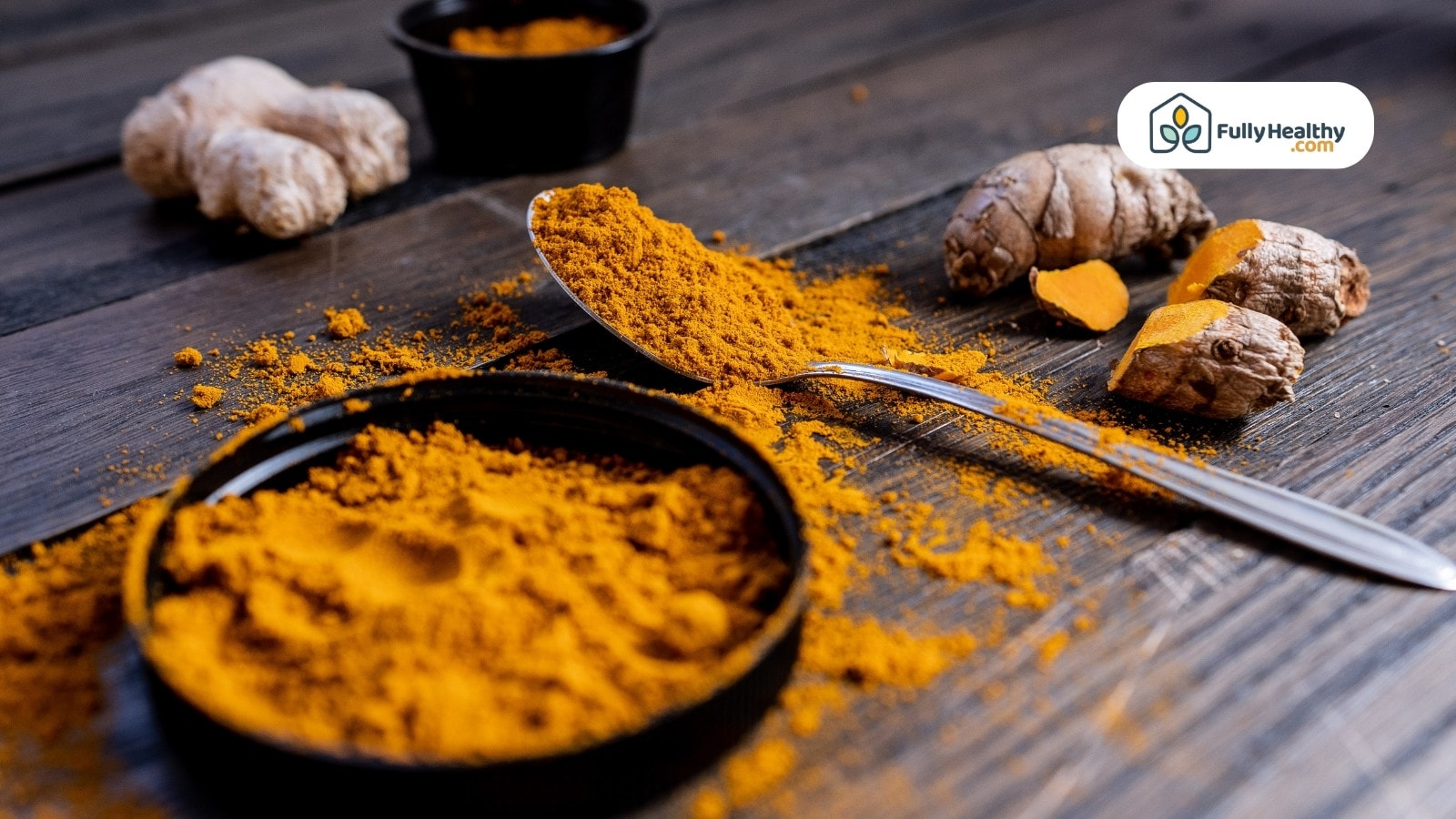 Spoonful of turmeric powder beside sliced and whole turmeric roots