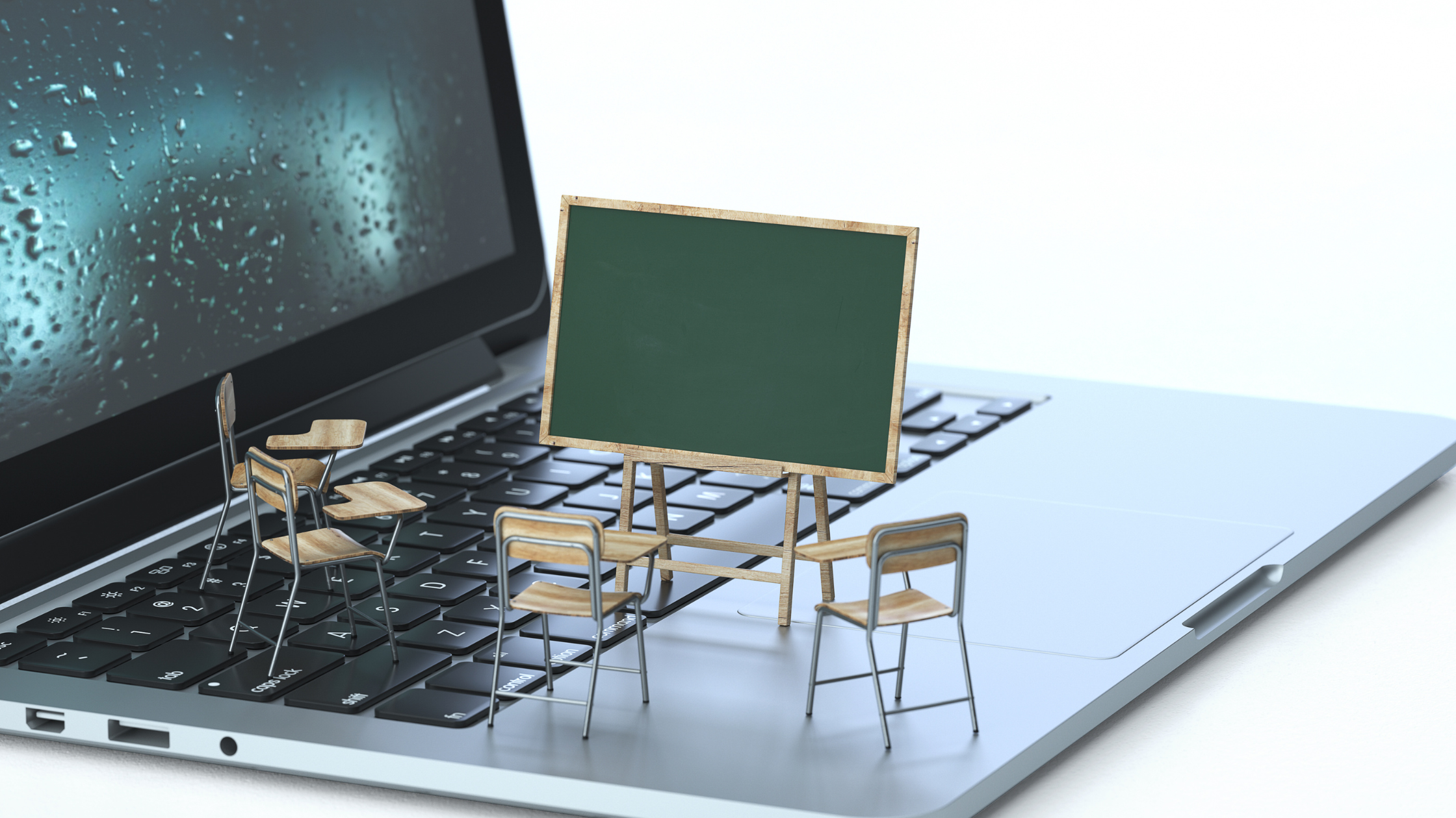 Miniature classroom setup with chairs and a blackboard on a laptop keyboard, illustrating online education and virtual learning.