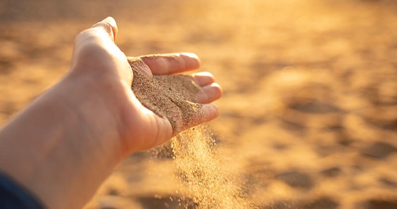 Hand holding sand as grains slip through the fingers, representing resilience.