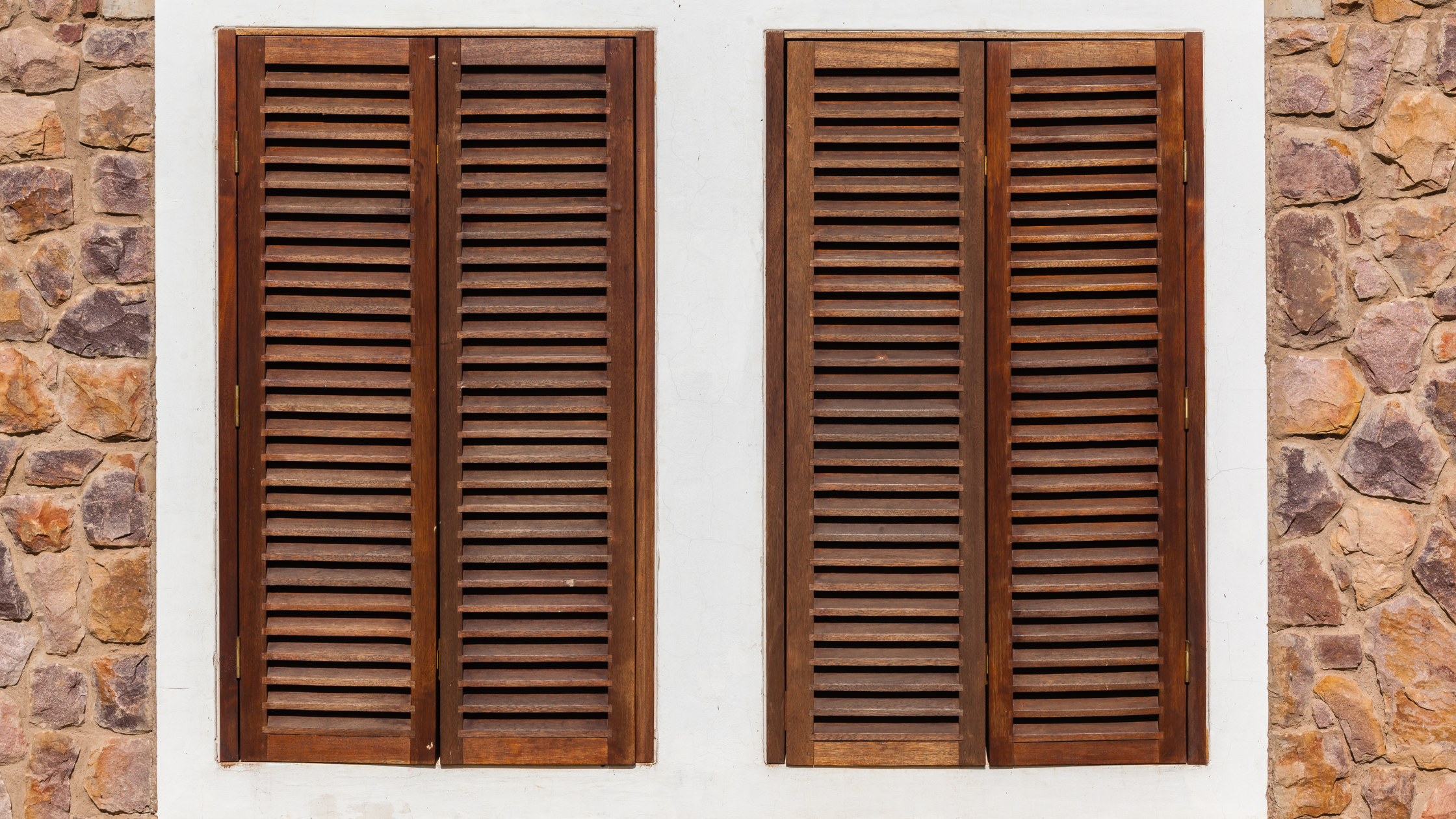 Outdoor wooden window shutters outside of rock building.