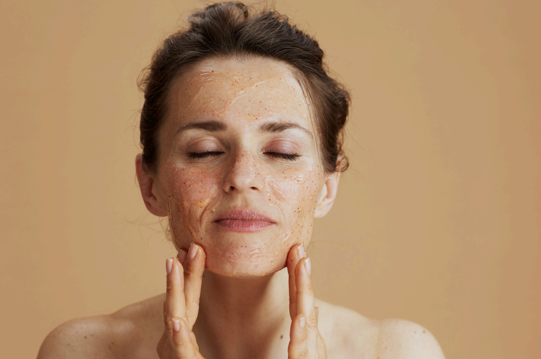Een vrouw met gesloten ogen masseert een gezichtsscrub in haar huid, met een ontspannen en verzorgde uitdrukking. Op het gezicht kun je licht scrubben. Op deze manier worden op het gezicht dode huidcellen verwijderd.
