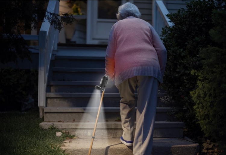 Elderly woman walking up steps with flashlight attached to cane