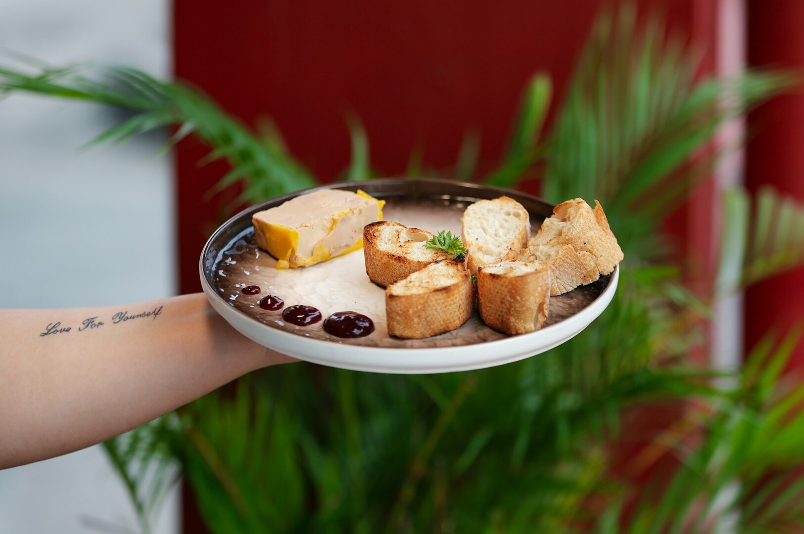 A hand presents a plate with assorted bread and cheese, highlighting a culinary offering from Singapore's dining scene.