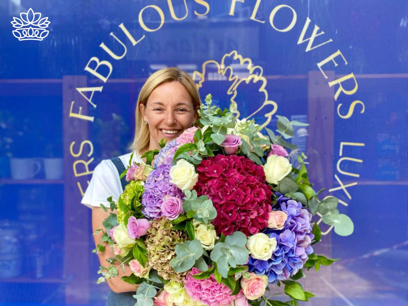 Beaming florist with an abundant congratulation flowers arrangement of hydrangeas, roses, and lush greens, symbolizing the joyful spirit of the Congratulations Flower and Gift Collection—Fabulous Flowers and Gifts.