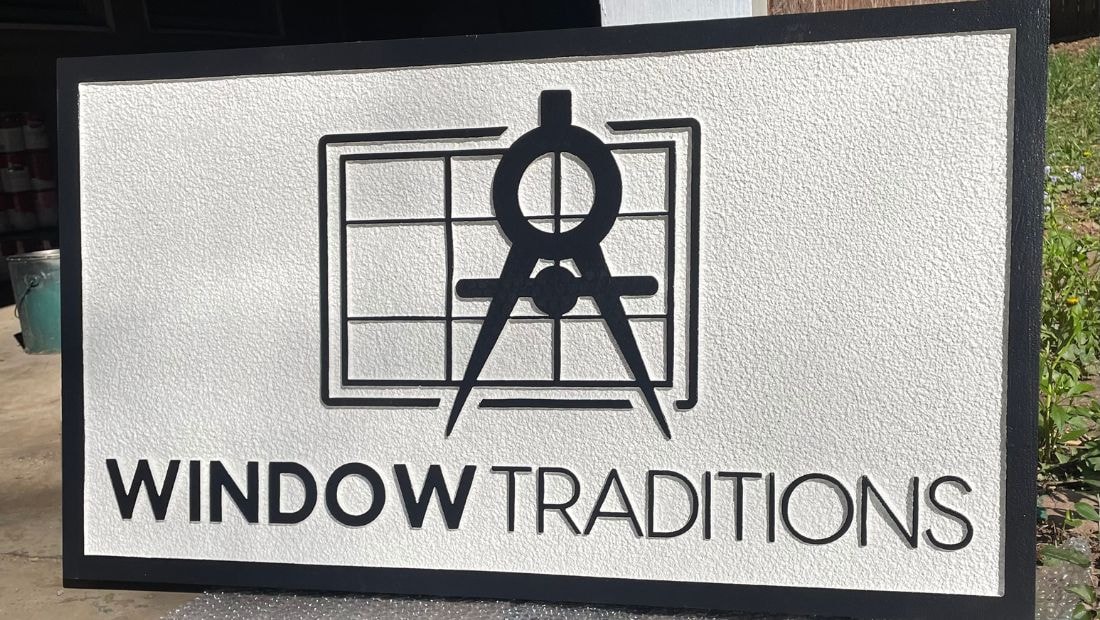 Custom dimensional sign for Window Traditions featuring a black architectural compass over a window grid design, with clean black raised lettering on a textured white background and a black border.