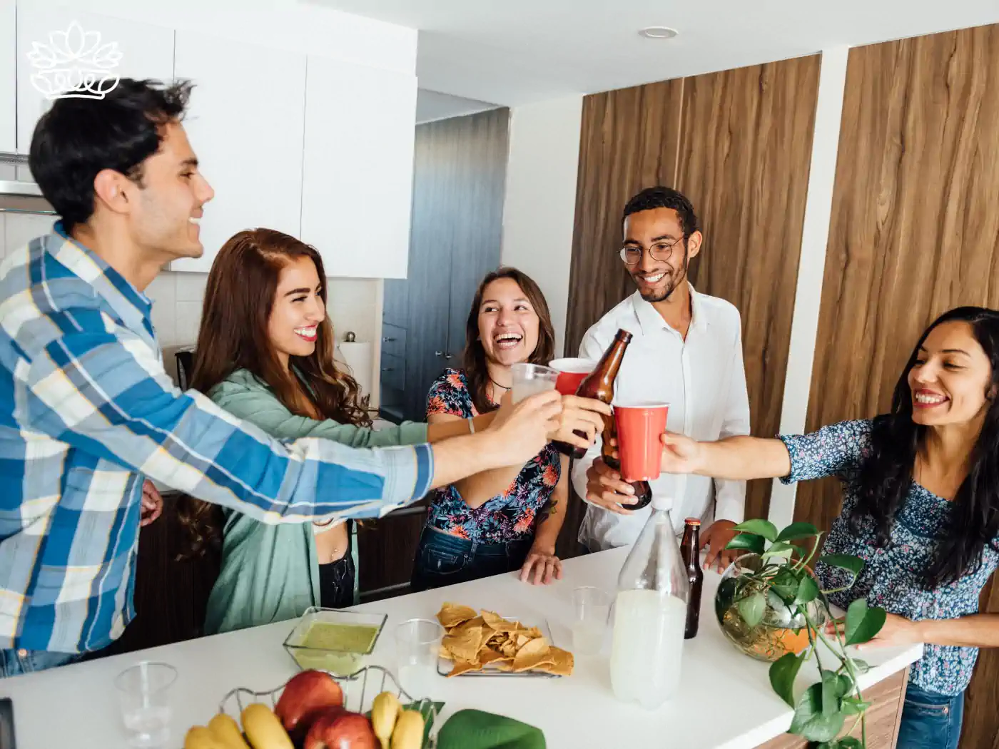 Friends toasting drinks at a lively housewarming party, sharing joy and laughter in a cozy kitchen. Fabulous Flowers and Gifts - Housewarming. Delivered with Heart.