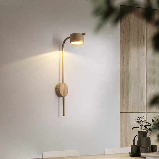 Modern wooden wall sconce with a cylindrical shade, casting warm light on a minimalist dining room wall; accompanied by simple decor and indoor plants.