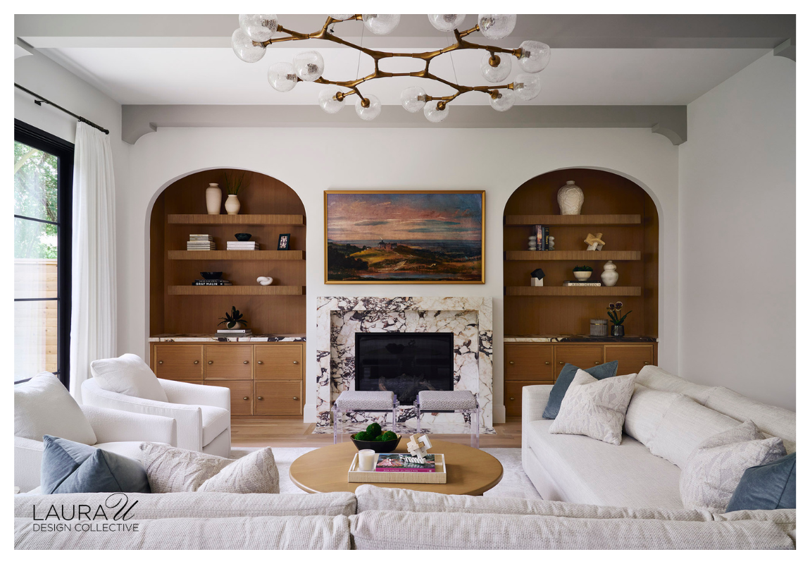 Modern living room with arched built-in bookcases, wood shelving, and a marble fireplace designed by Laura U Design Collective.
