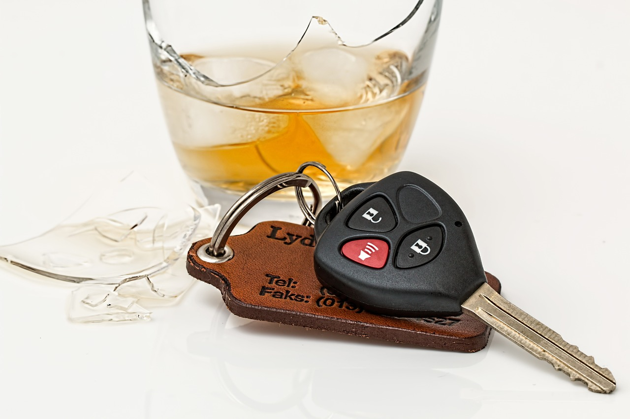 An image of a broken drinking glass filled with an alcoholic beverage beside a set of car keys.