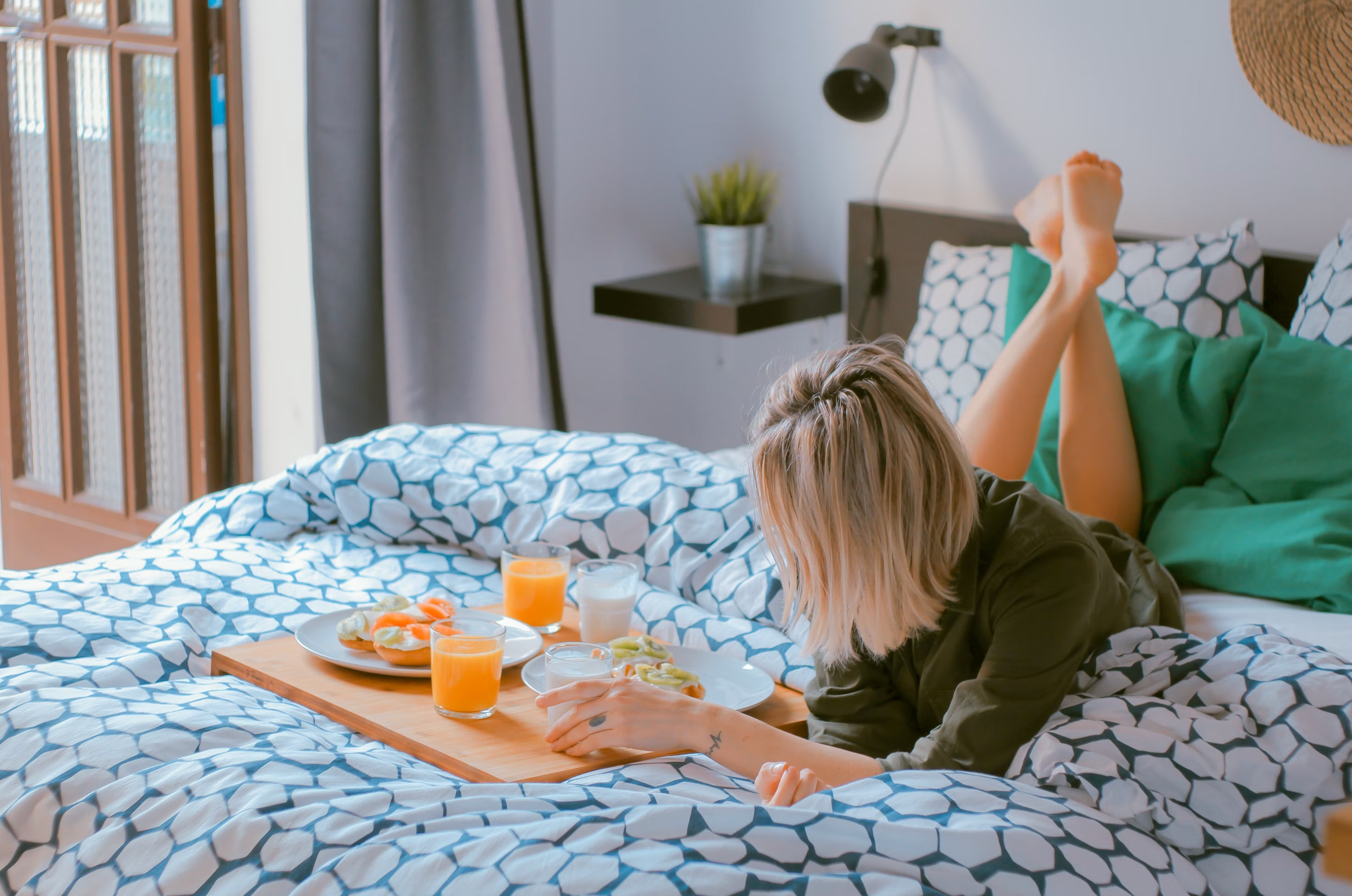 A woman with blond hair enjoying breakfast in bed with orange juice in a well-light, clean bedroom