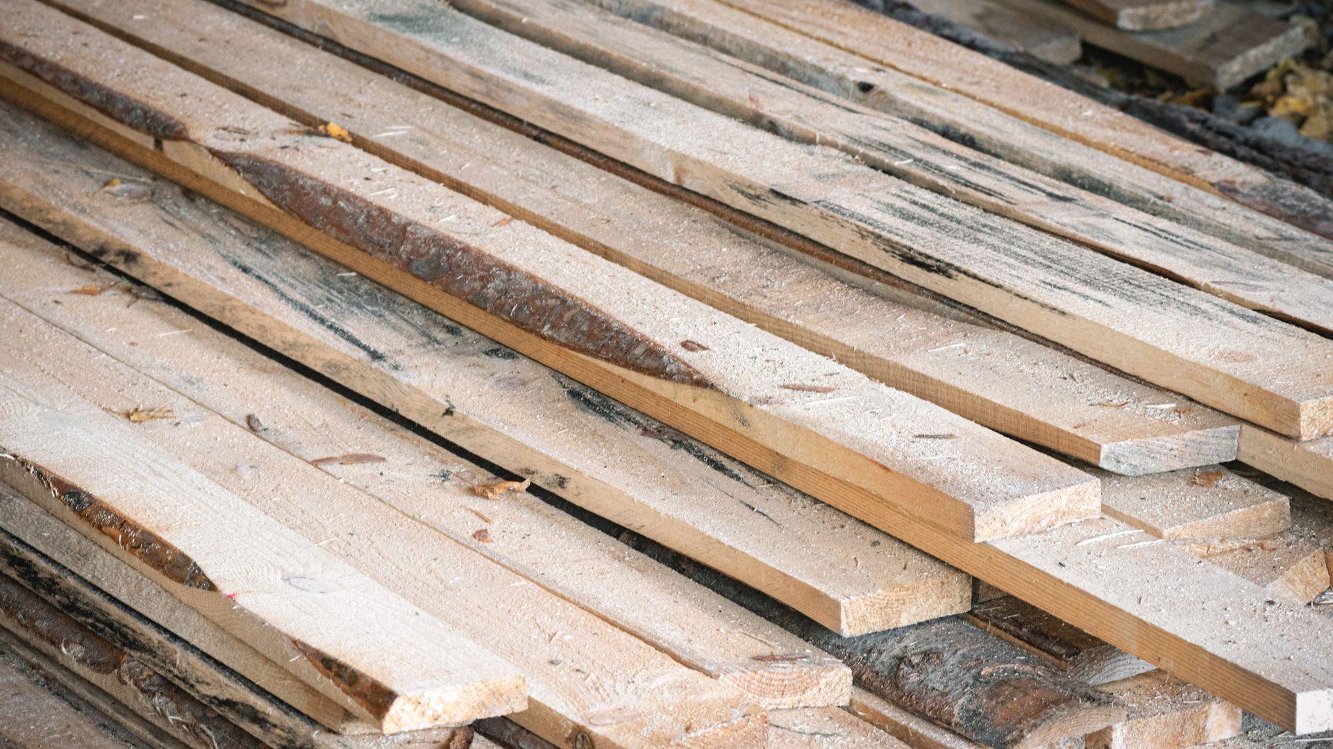 A stack of dimensional lumber with bark and stains.