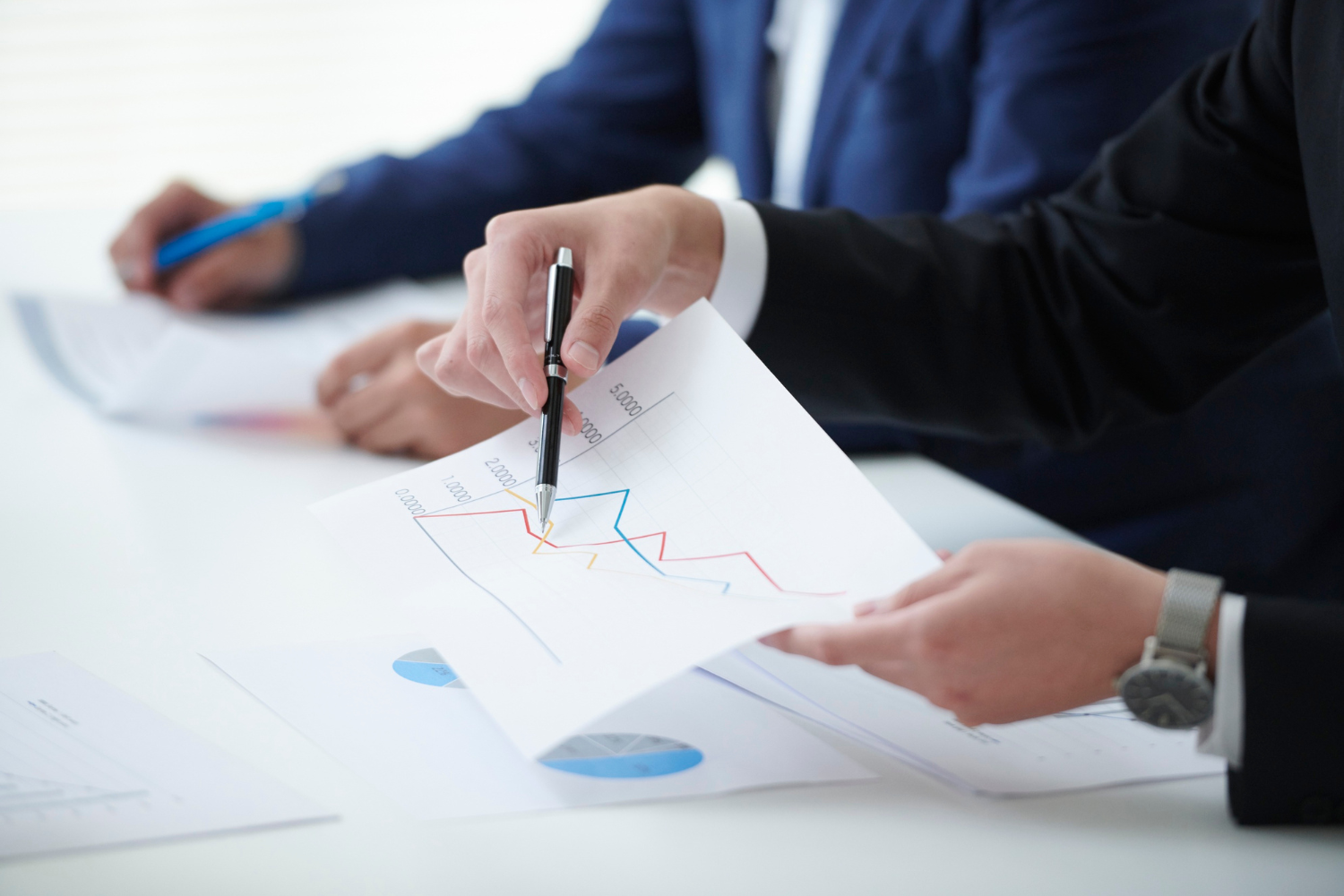 Two business people are sitting at a table with papers and pens.