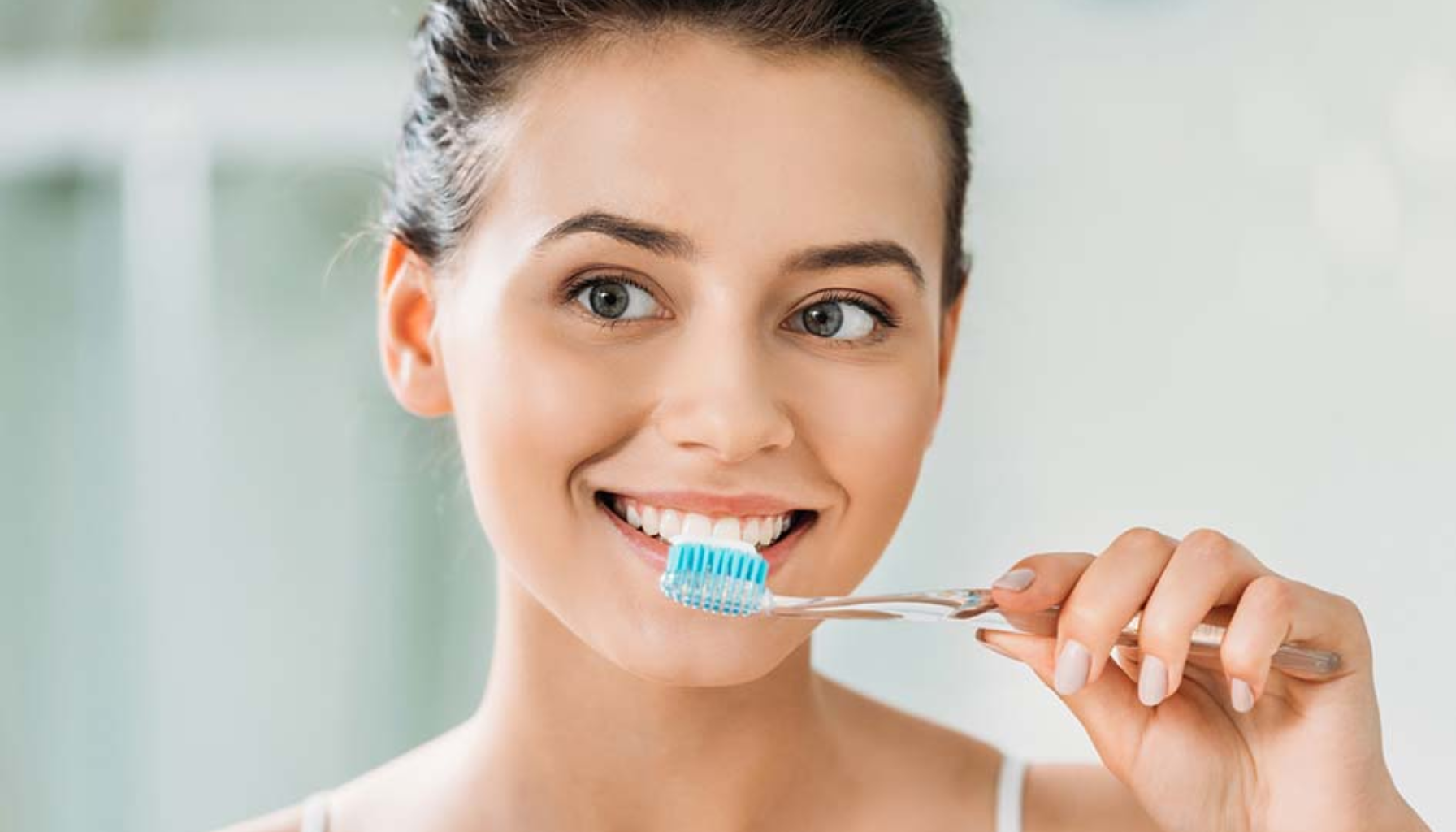 Tannsjekk: Grunnlaget for et sunt smil 15 Kvinne smiler mens hun pusser tennene med blå tannbørste, viser god tannhygiene og sunne vaner.