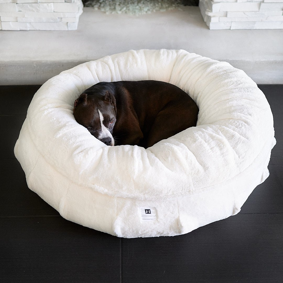 A white donut dog bed with faux fur and a high bolster design