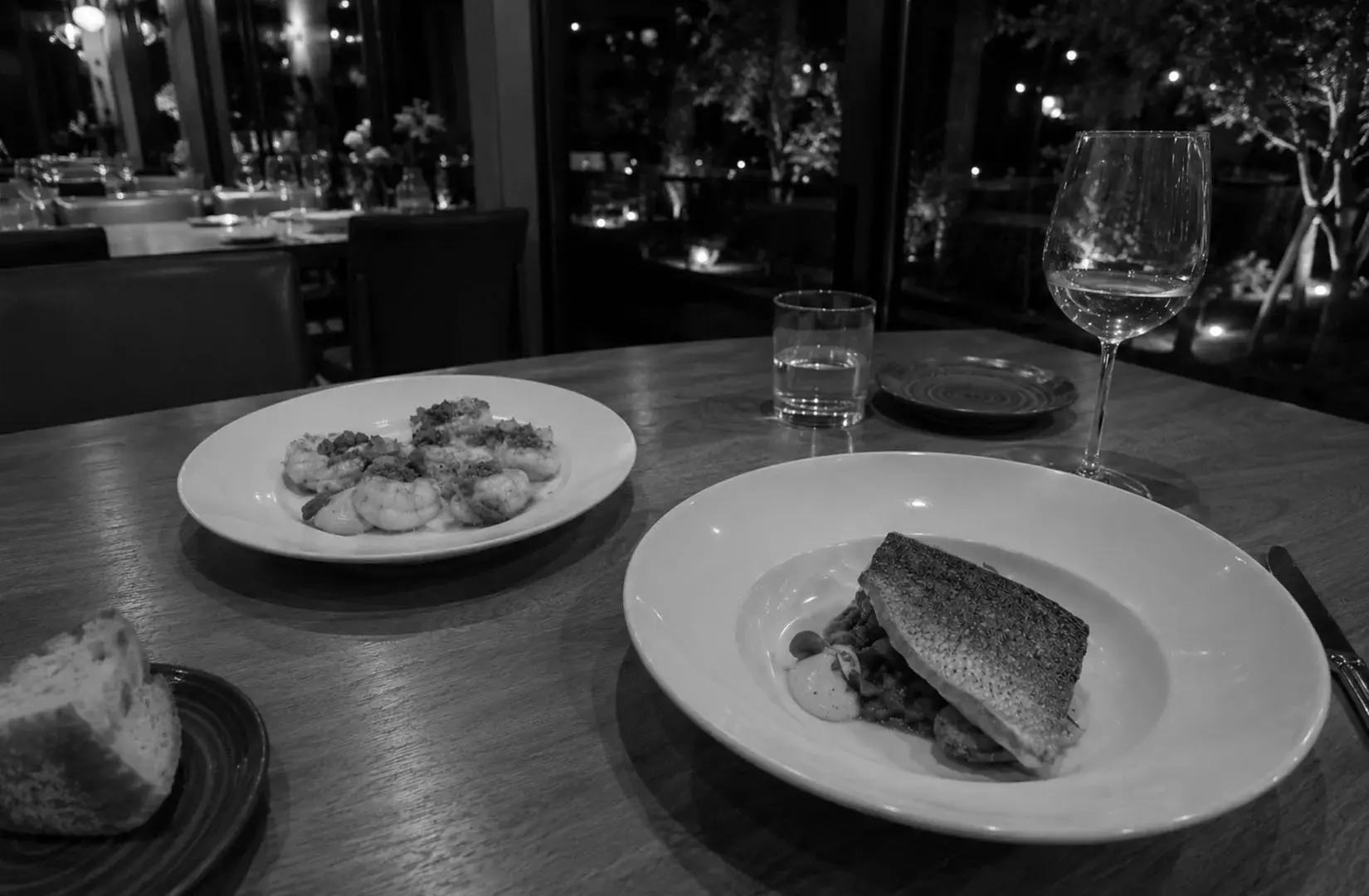 Seared fish and shrimp dishes served on a wooden table in a cozy restaurant setting.
