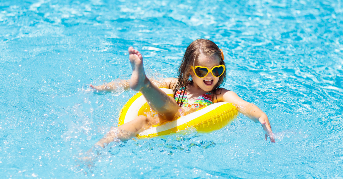 Young girl wearing heart-shaped sunglasses playing in a bright blue swimming pool, representing family-friendly amenities at The Pointe at Moores Inlet in North Wildwood.