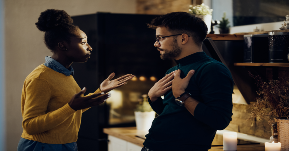 A photograph of a couple standing in a kitchen, with one partner looking upset and the other appearing defensive. The couple appears to be in the midst of an argument or disagreement, possibly related to household chores or responsibilities. The image conveys the idea of a couple who may be experiencing difficulties in their relationship and could benefit from the services of a certified Gottman Method Couples Therapist in New York City. The therapist can help the couple to develop effective communication skills, build emotional connection, and reduce conflict in their relationship, even in everyday situations like household chores.