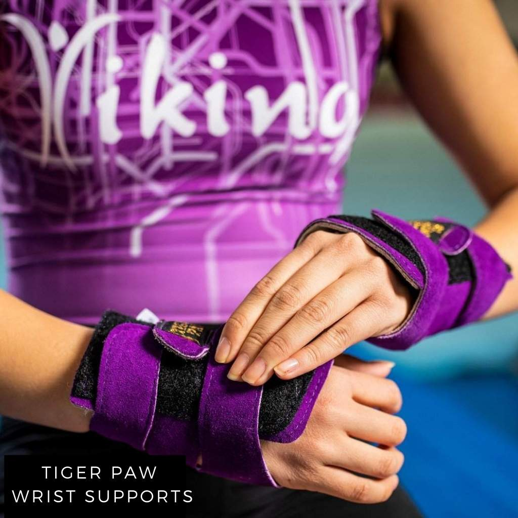 Young gymnast wearing purple tiger paw wrist supports and purple leotard.