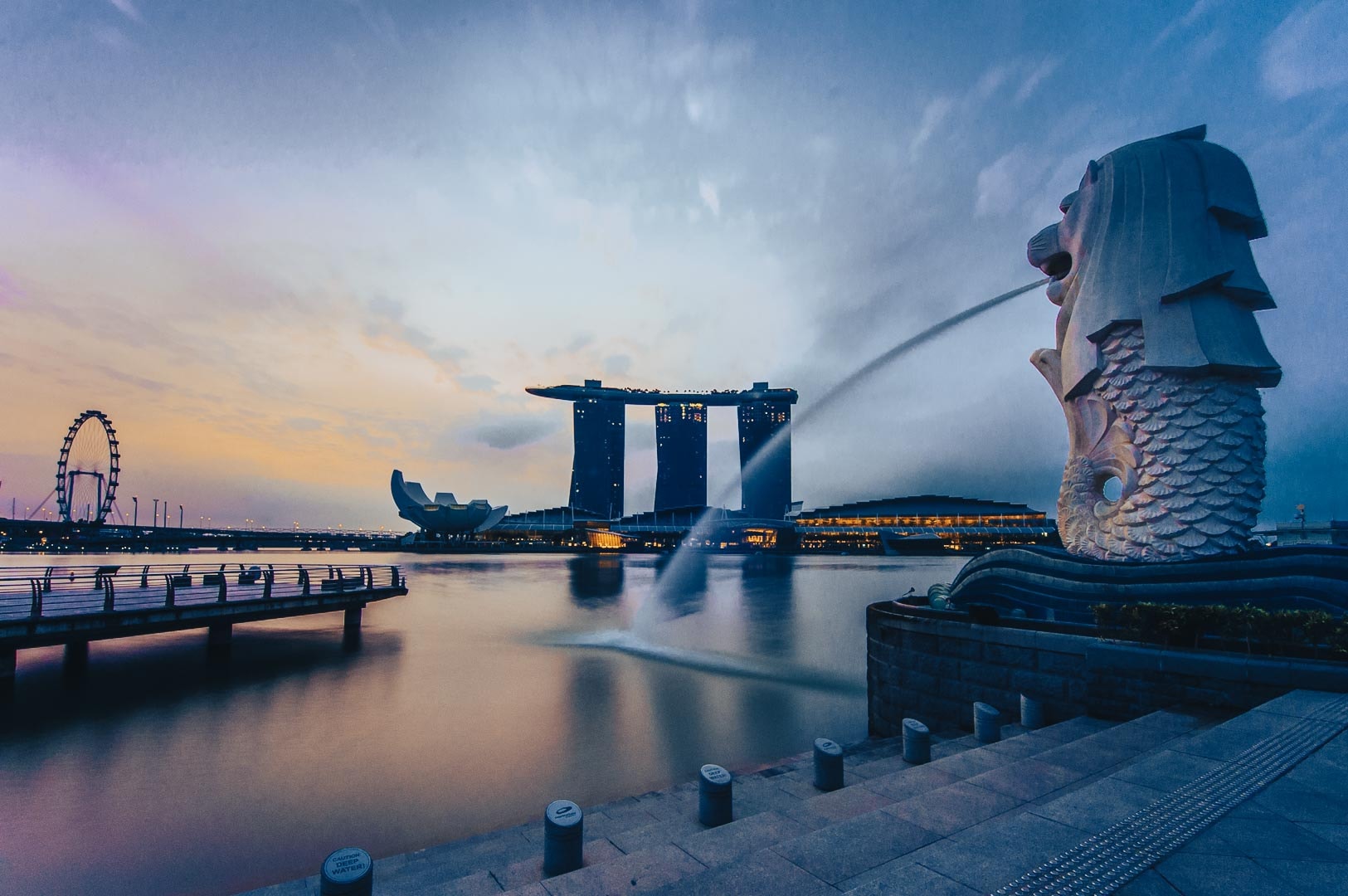 Merlion statue overlooking Marina Bay with Marina Bay Sands and the Singapore Flyer in the background at blue hour.
