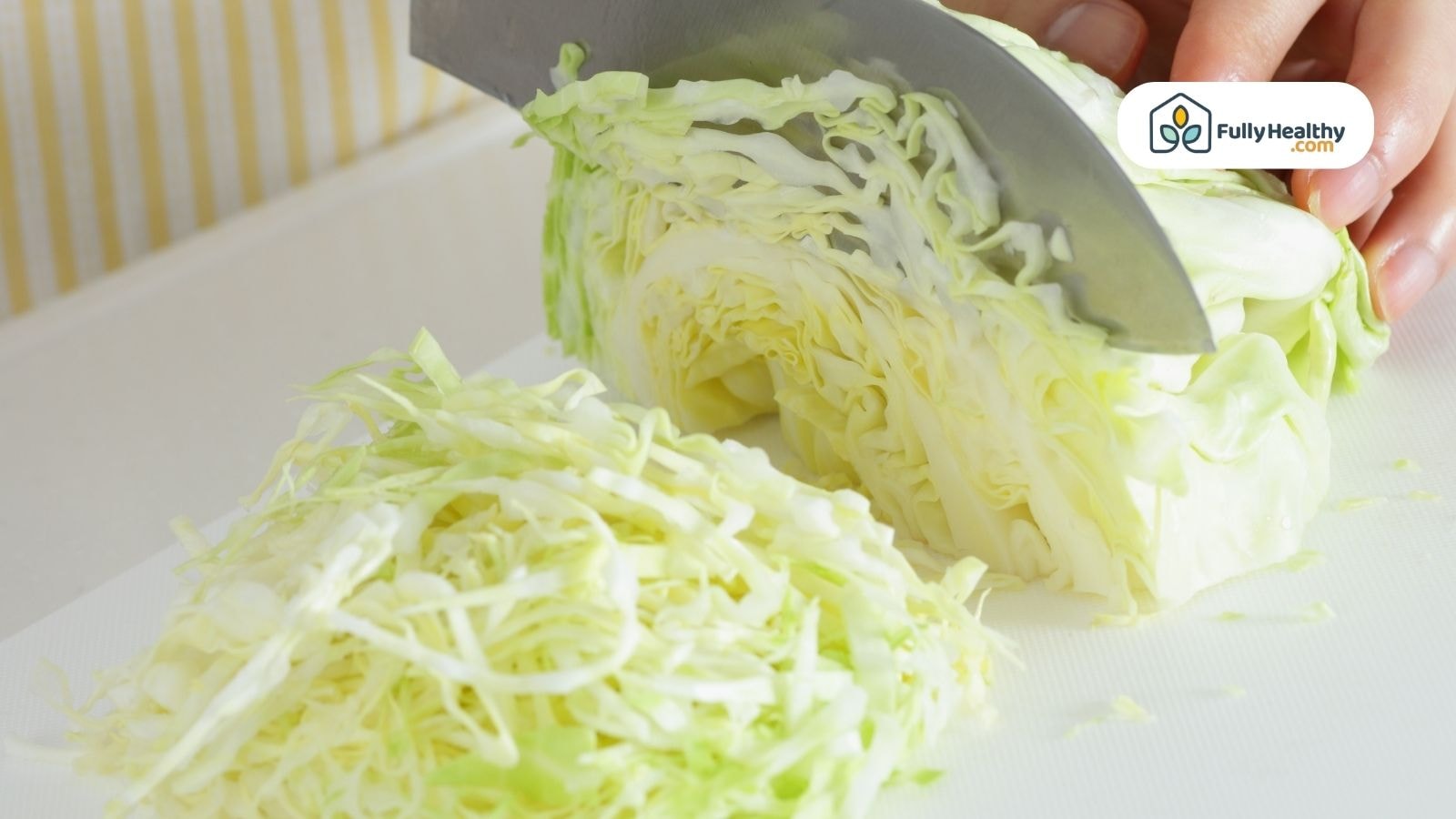 Shredded green cabbage being sliced on a white cutting board