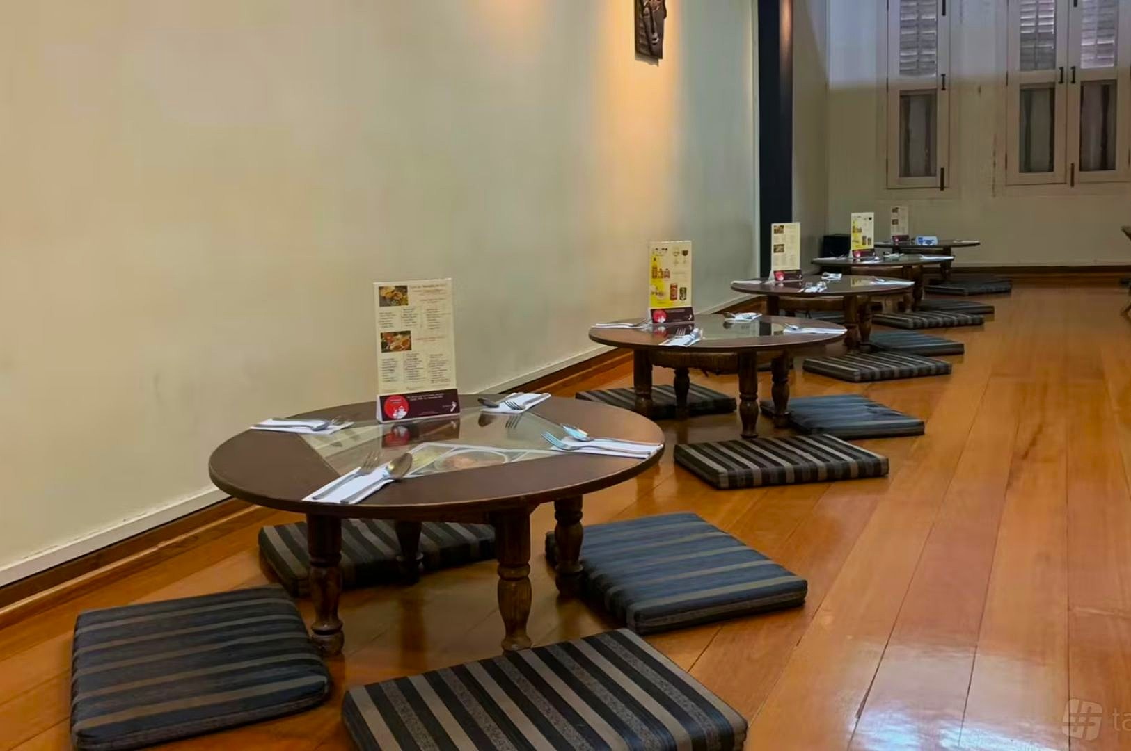 Low wooden tables with menus and striped cushions are arranged along a wall in a minimalist restaurant with a warm, inviting ambiance.