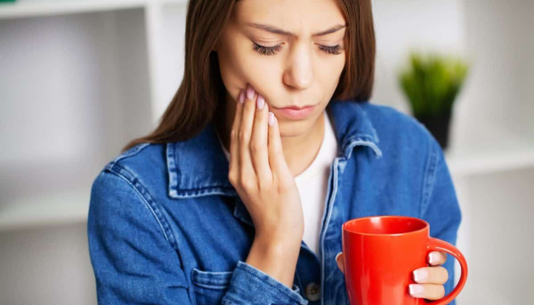 Kaffe etter tanntrekking: Hvorfor du bør vente litt med favorittkoppen 9 Kvinne med tannverk som holder en kopp, med smerte i kinnet og tydelig ubehag i ansiktet.