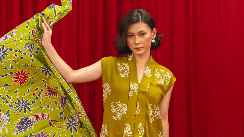 A person in a yellow dress holding a green batik cloth