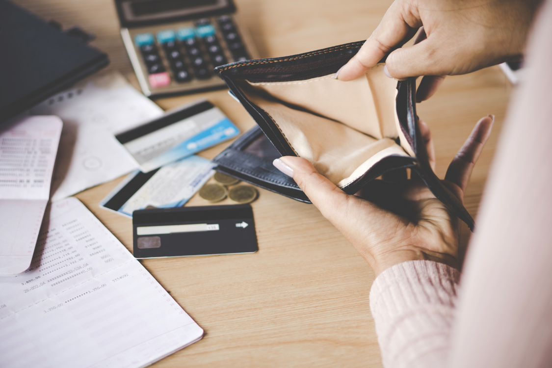 Open wallet with no cash surrounded by credit cards and receipts, representing the financial strain of selling a business without help.