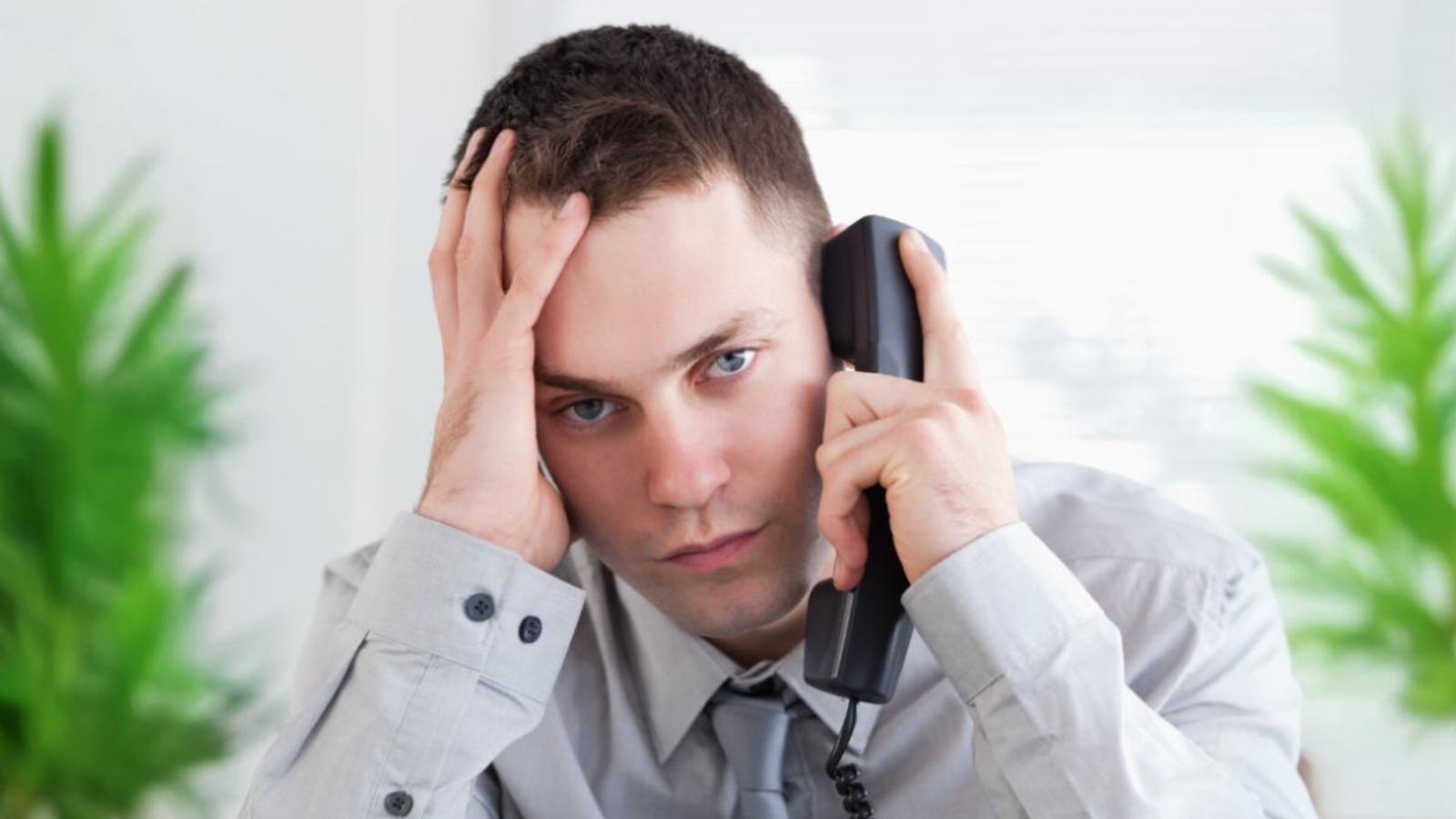 Stressed man holding a corded phone, representing the inefficiency and limitations of outdated systems that fail to meet modern business needs.