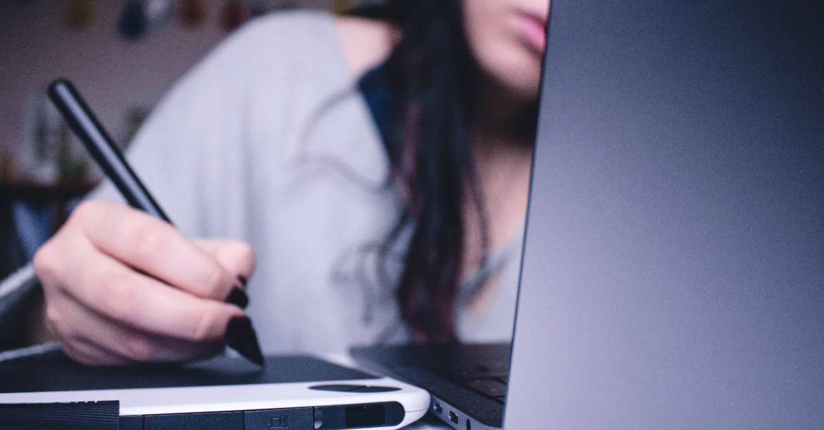 Vrouw zit voor laptop en werk op een tablet met een stylus.