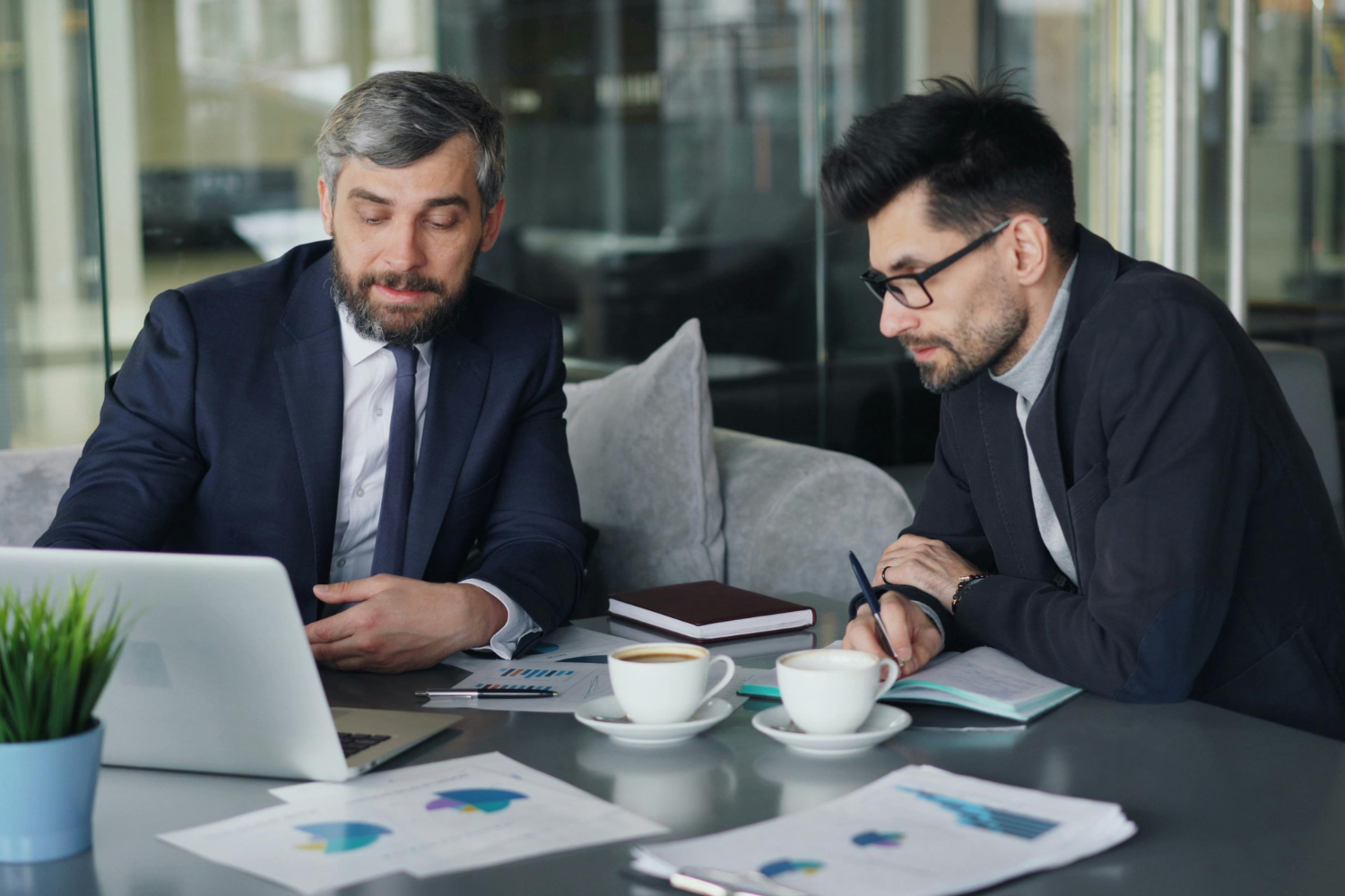 People in suits sitting at a table looking at a laptop.