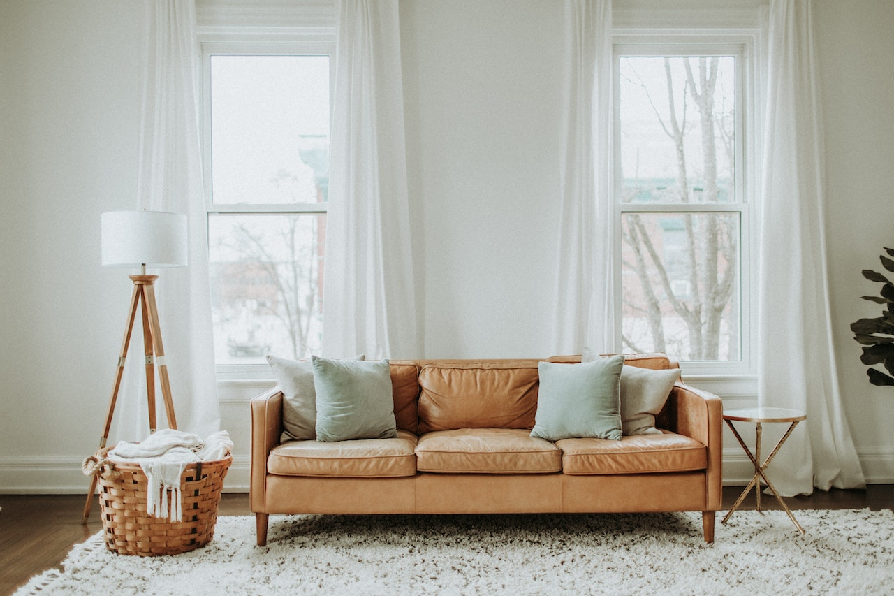 tan leather sofa tripod lamp in airy living room - image credit: https://www.pexels.com/photo/white-and-brown-sofa-chair-near-white-window-curtain-6480707/