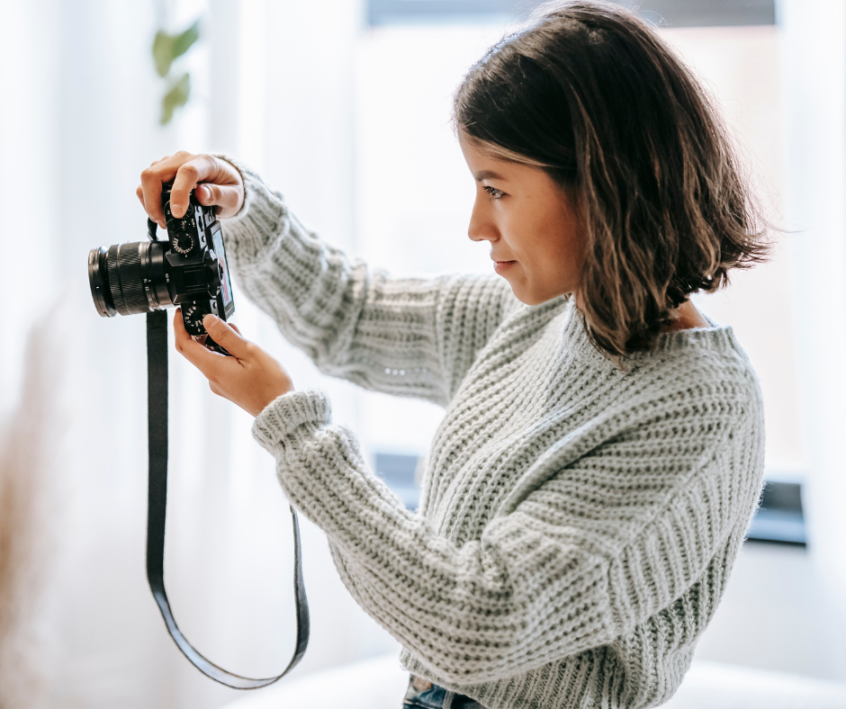 Woman in a pale blue sweater taking photos with a camera.