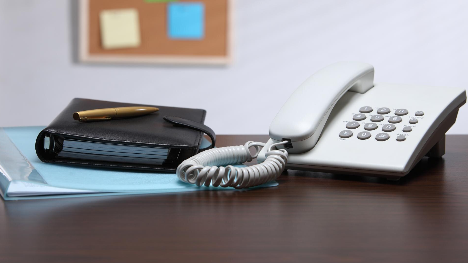 Desk with a corded office phone, planner, and pen, representing traditional telephony before POTS replacement.