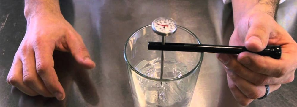 A digital thermometer being used to measure the temperature of ice water