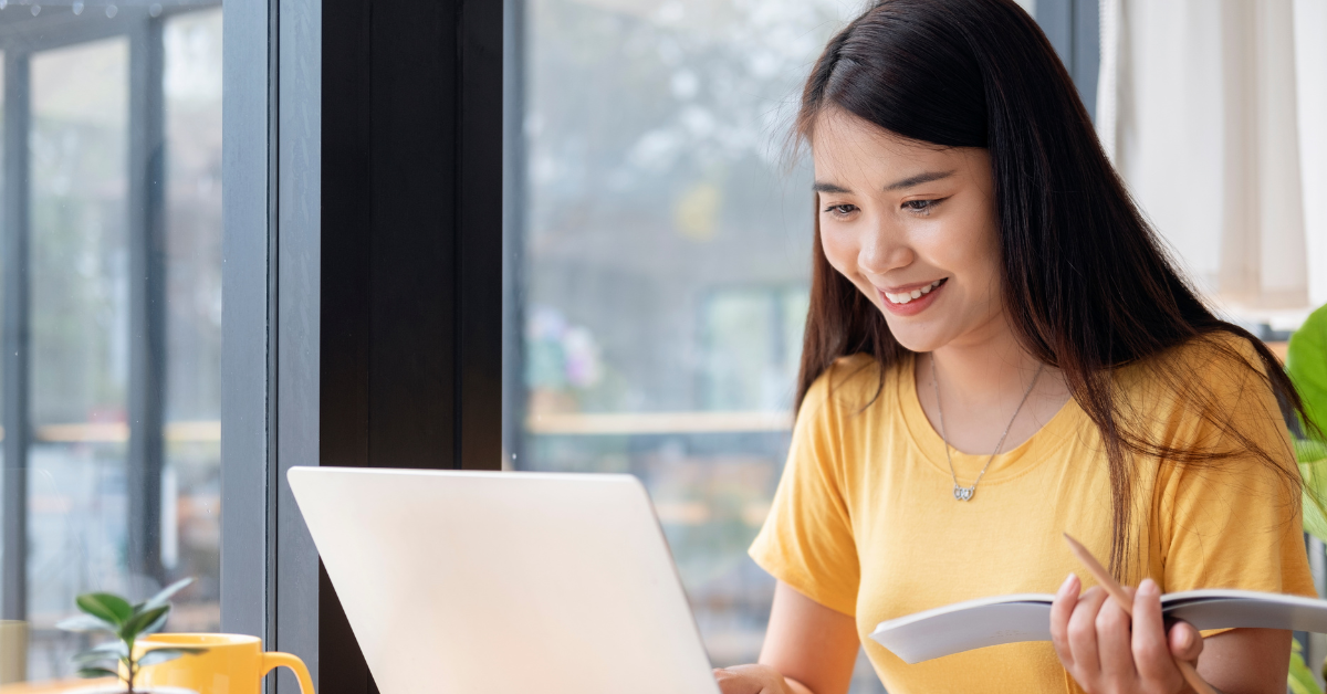 A smiling woman working on a laptop near a window, showcasing convenience and affordability with affordable tax service.