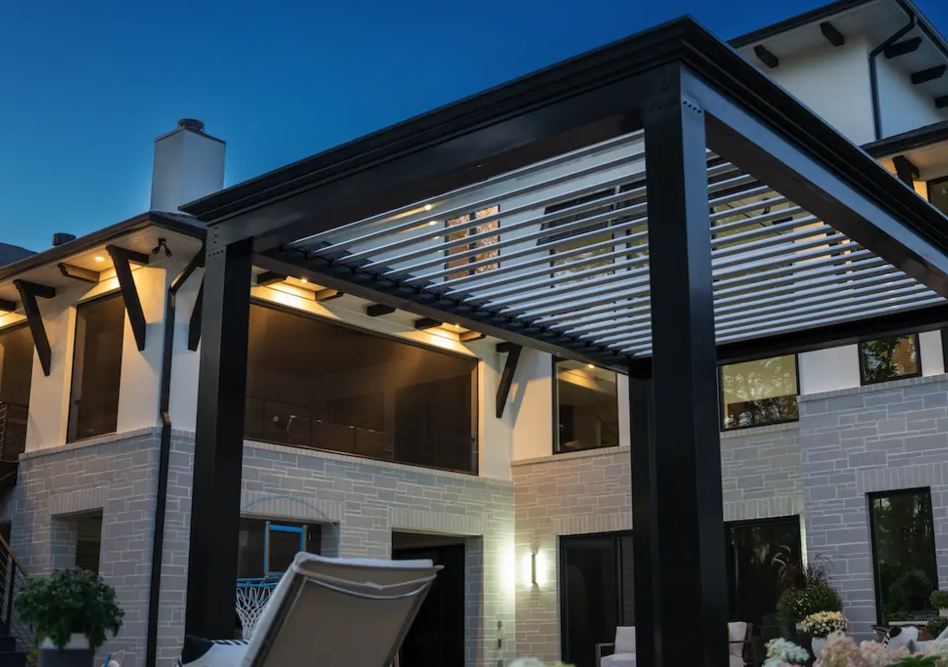 A black pergola installed in a backyard by a pool.