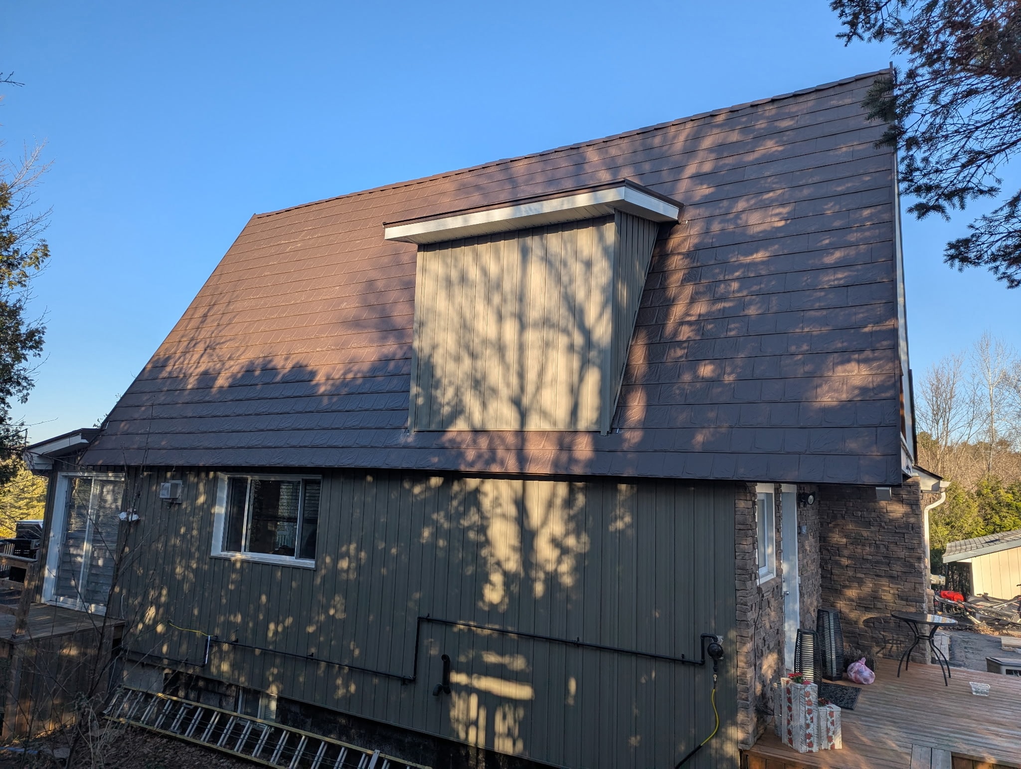 Steep-sloped residential roof featuring brown Armadura metal shingles installed by Roof Pros Plus, highlighting durable steel panels and a unique architectural design against a clear blue sky.