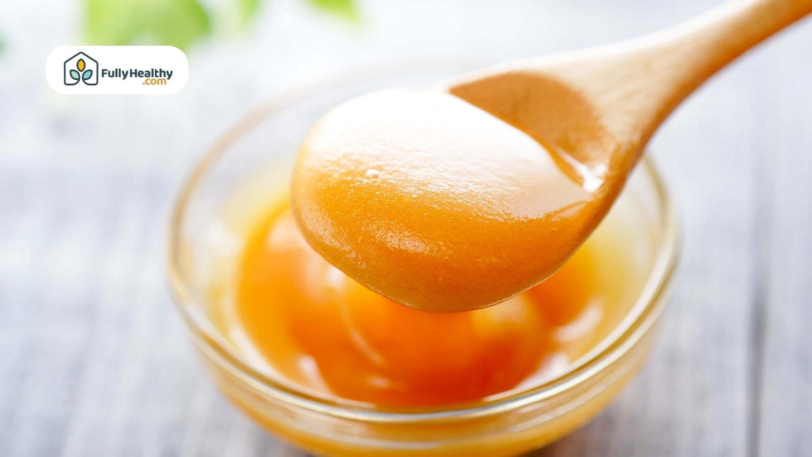 Wooden spoon scooping thick golden Manuka honey from bowl