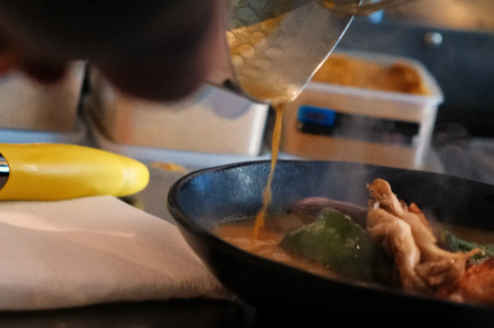 A person pouring a liquid over a dish in a restaurant kitchen.