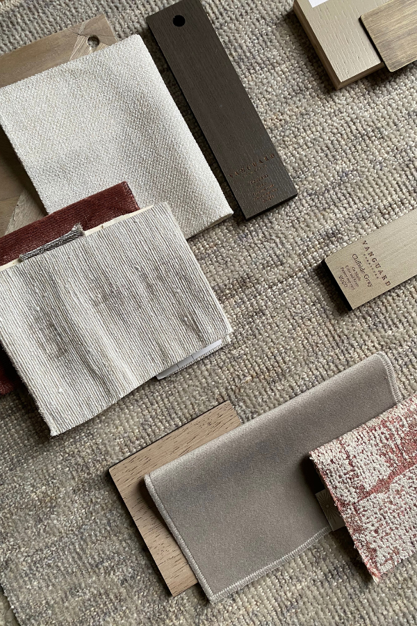 Neutral fabric swatches and wood finish samples arranged on a textured beige rug.