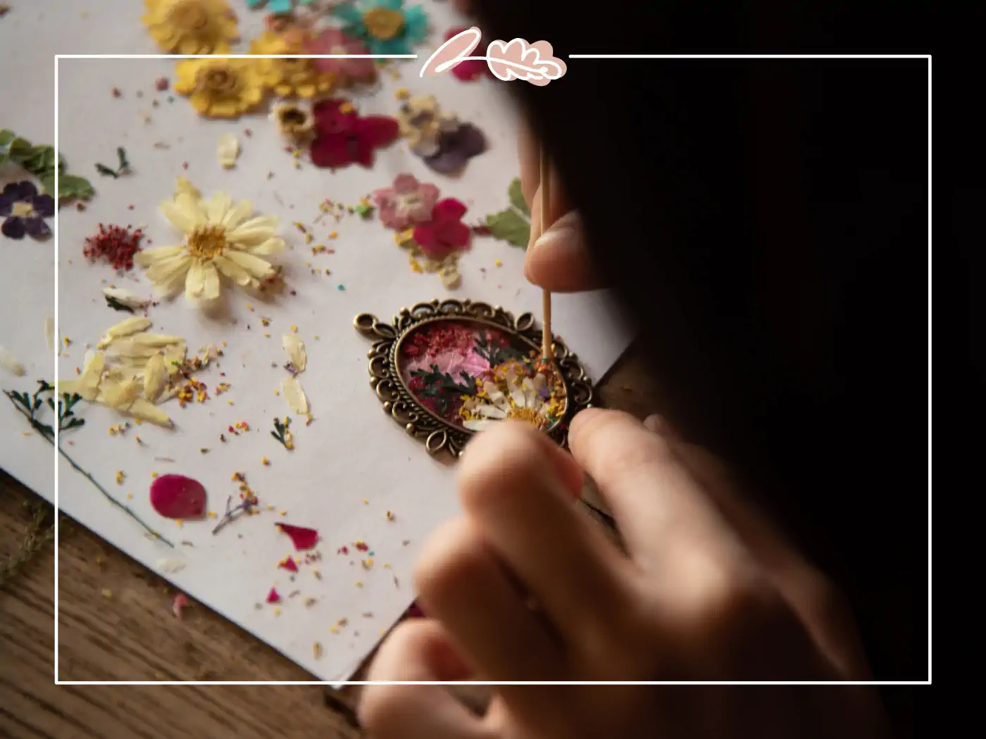 Person decorating a pendant with dried flowers on a piece of paper, Fabulous Flowers and Gifts